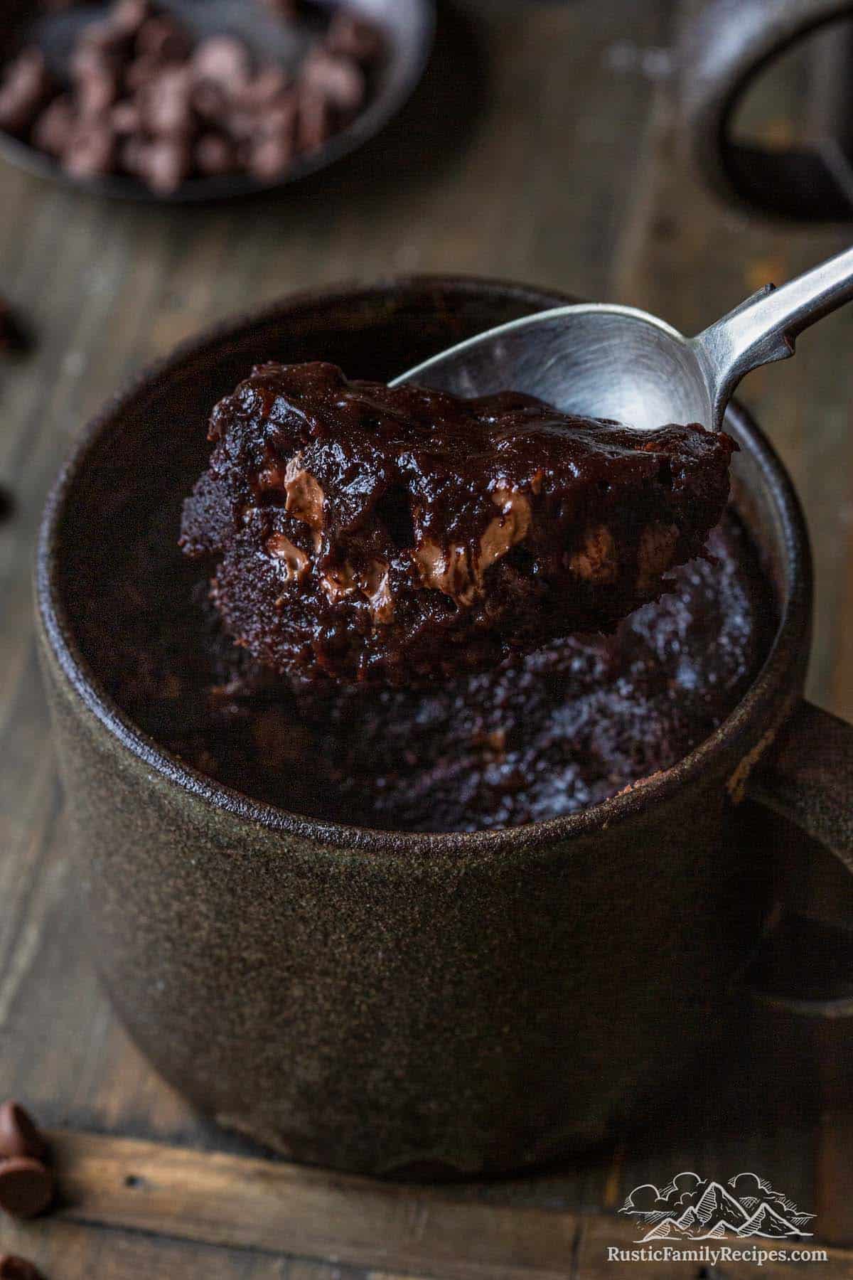 A spoon with a scoop of brownie in front of a mug