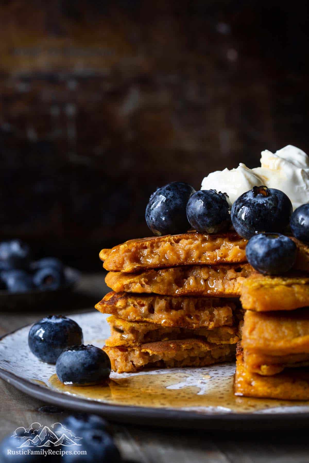 Stack of pumpkin pancakes with blueberries and whipped cream, with a slice taken out