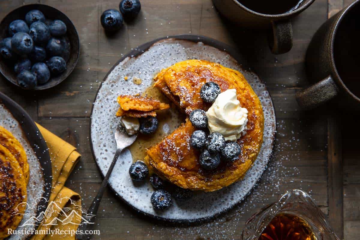 A stack of pancakes with blueberries, whipped cream and powdered sugar, top view