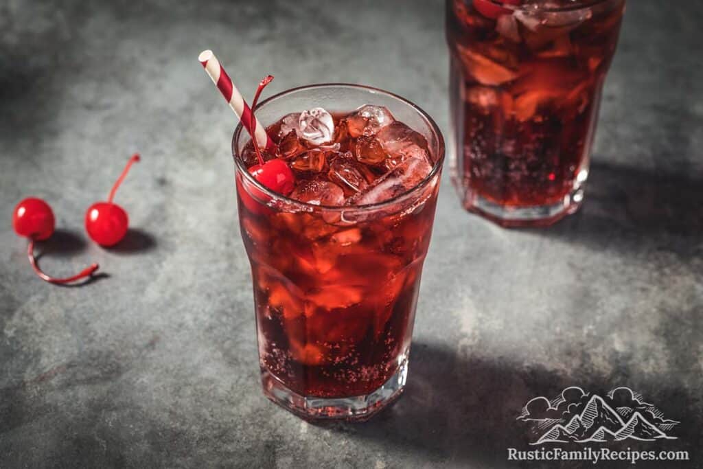 Two glasses filled with coca cola, ice and topped with cherries