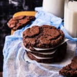 A stack of chocolate cookies next to glasses of milk