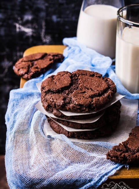 A stack of chocolate cookies next to glasses of milk