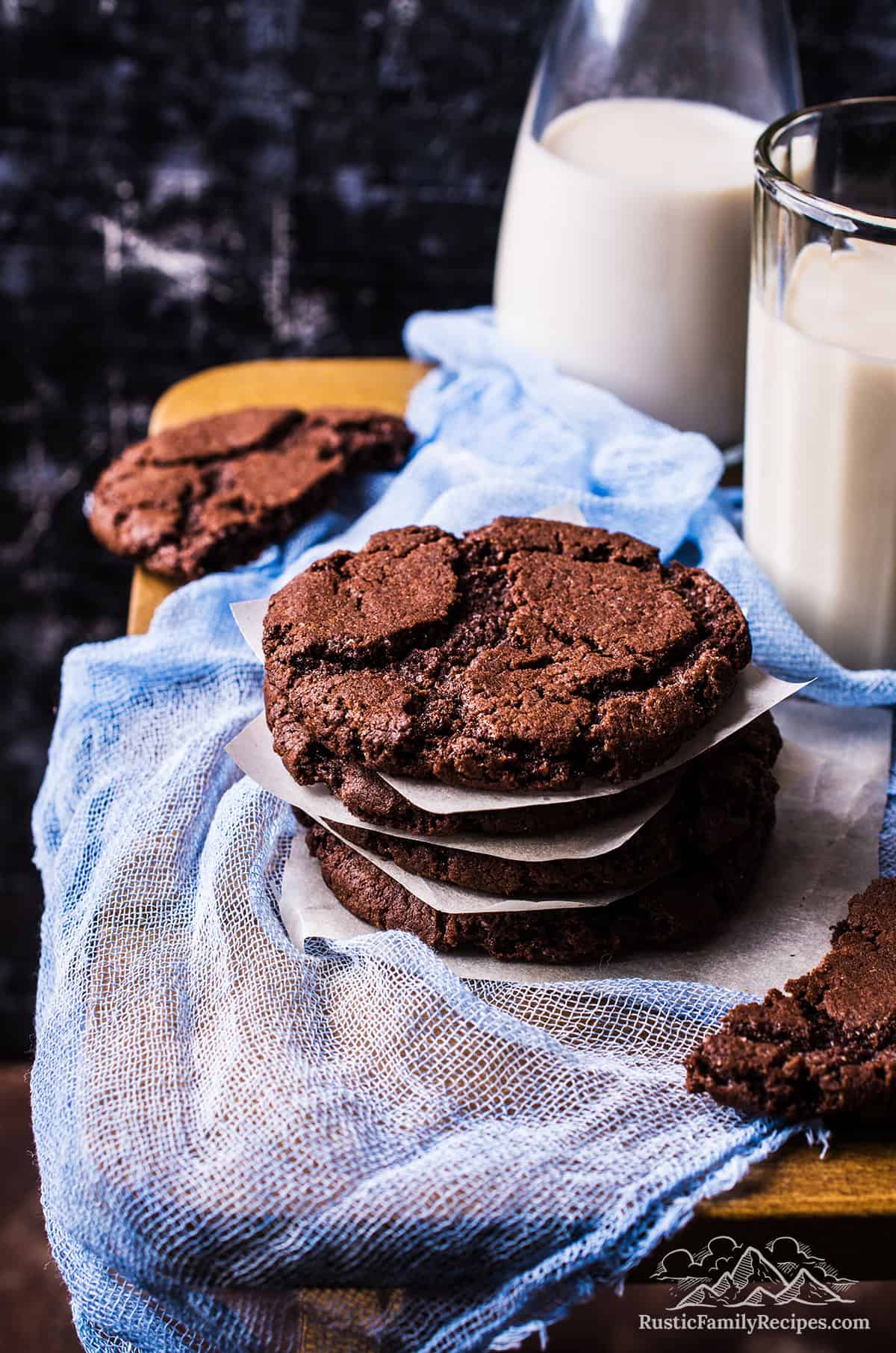 A stack of chocolate cookies next to glasses of milk