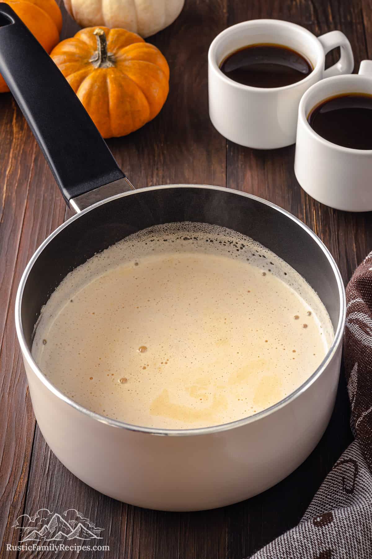 Pumpkin spice milk in a small pot next to two cups of coffee