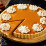 Pumpkin tart with a slice cut and dollops of whipped cream