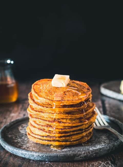 Stack of pumpkin johnnycakes with butter and syrup