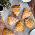 Five pumpkin scones on parchment paper next to a cup of coffee