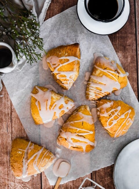 Five pumpkin scones on parchment paper next to a cup of coffee
