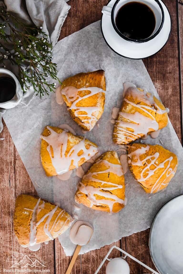 Five pumpkin scones on parchment paper next to a cup of coffee