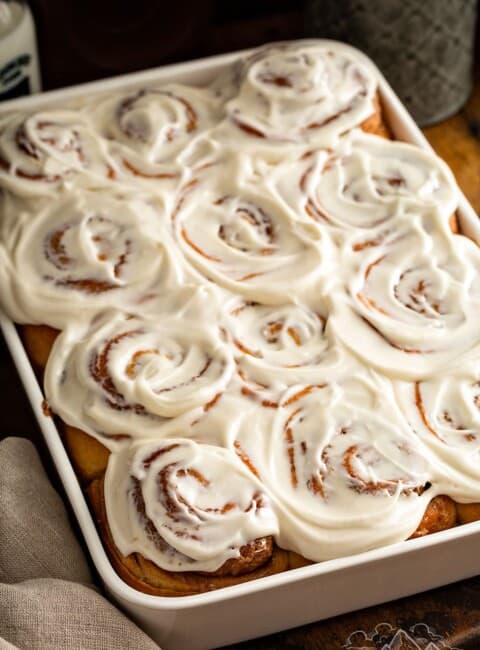 A white baking dish with frosted cinnamon rolls freshly baked.