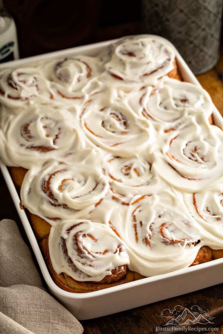 A white baking dish with frosted cinnamon rolls freshly baked.