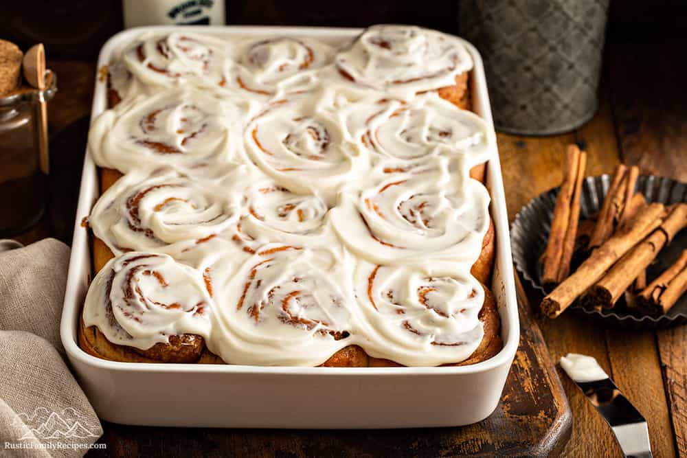 A white baking dish with frosted homemade cinnamon buns