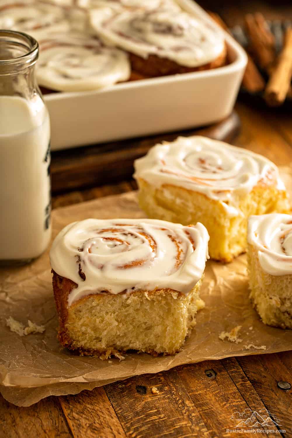 Three cinnamon rolls in front of a baking dish and a jar of milk