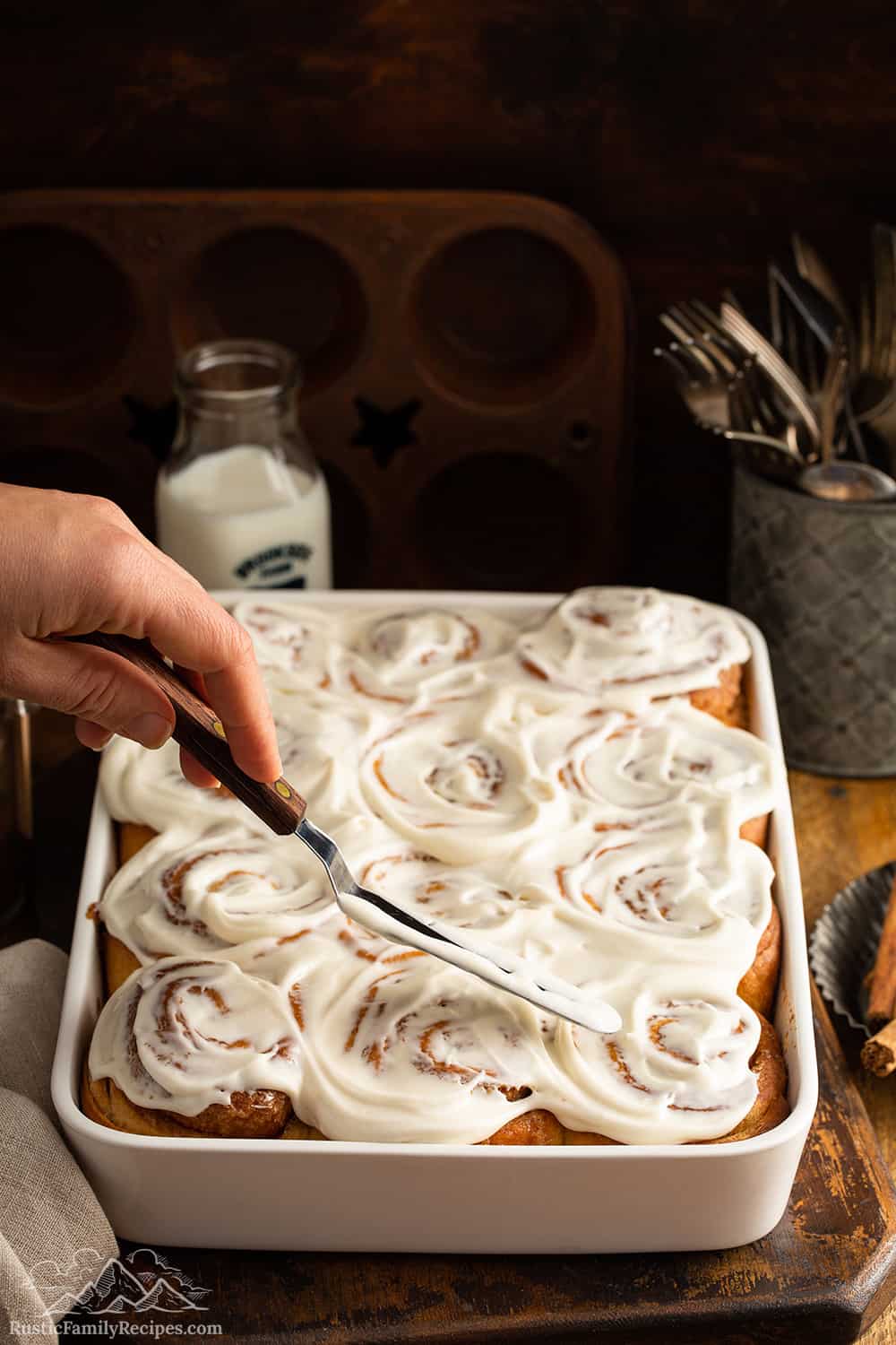 Freshly baked cinnamon rolls being frosted.