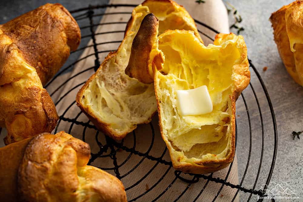 A pile of popovers, one sliced with melted butter inside.