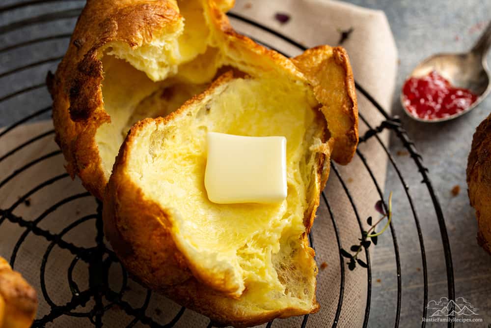 Sliced open popover with melting butter, next to a spoonful of jam.