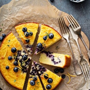 Fluffy homemade blueberry coffee cake on parchment paper next to a bowl of blueberries.