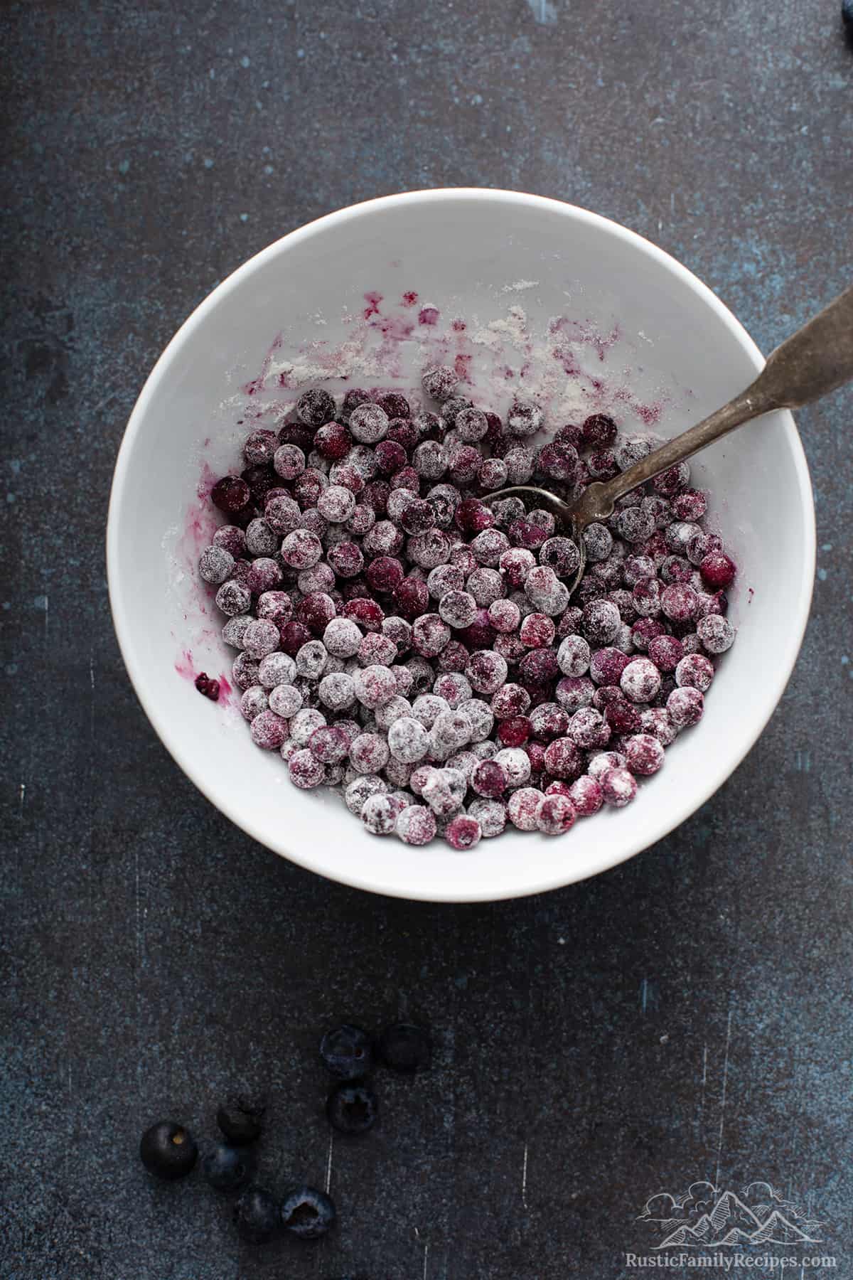 A white bowl with frozen blueberries tossed with flour mixture