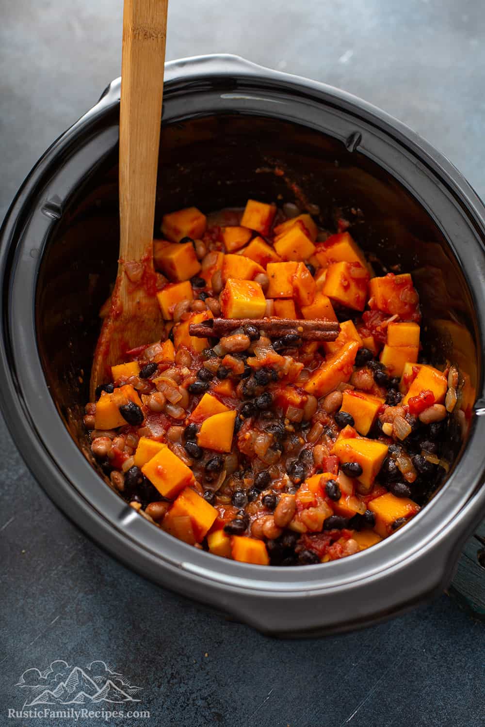 A slow cooker with diced butternut squash, beans and spices for vegetarian chili.