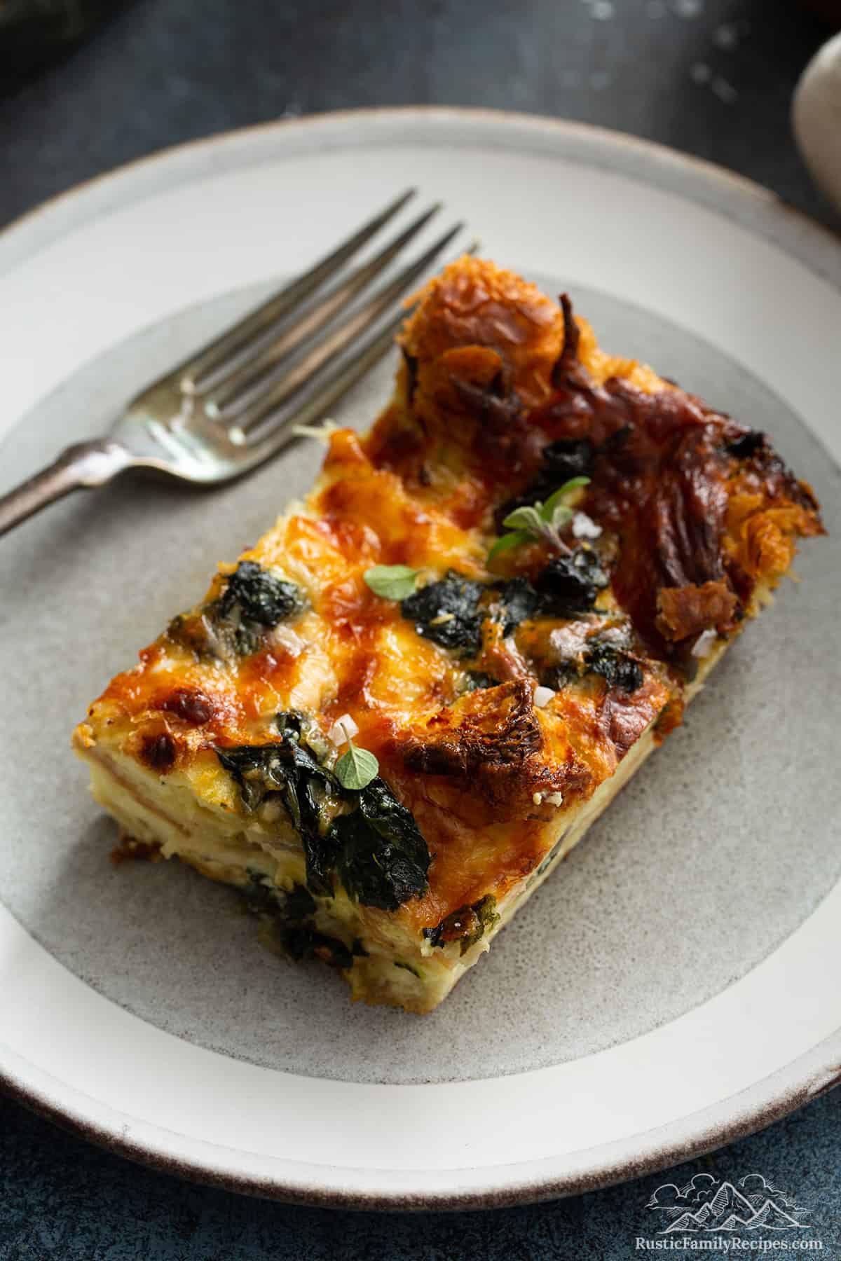 A slice of spinach strata on a plate with a fork