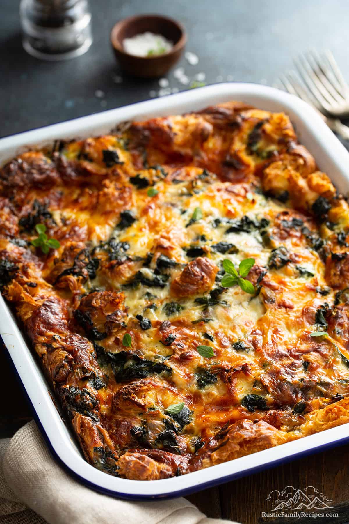 A baked spinach strata in a white baking dish on a wood counter
