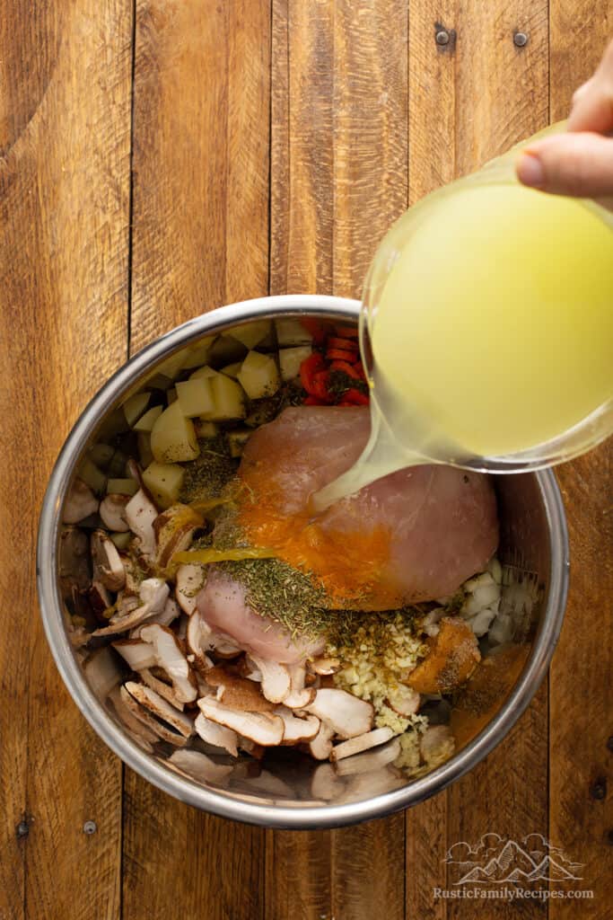 Pouring broth into an instant pot bowl with chicken soup ingredients.