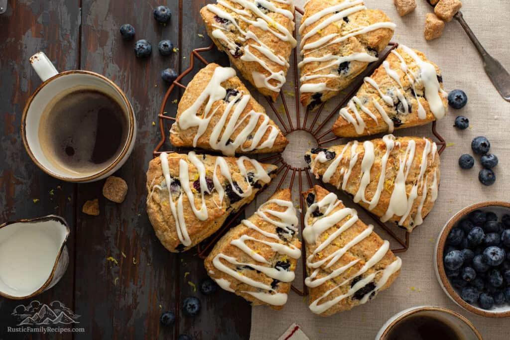 Glazed blueberry scones on a cooling rack next to a cup of coffee.