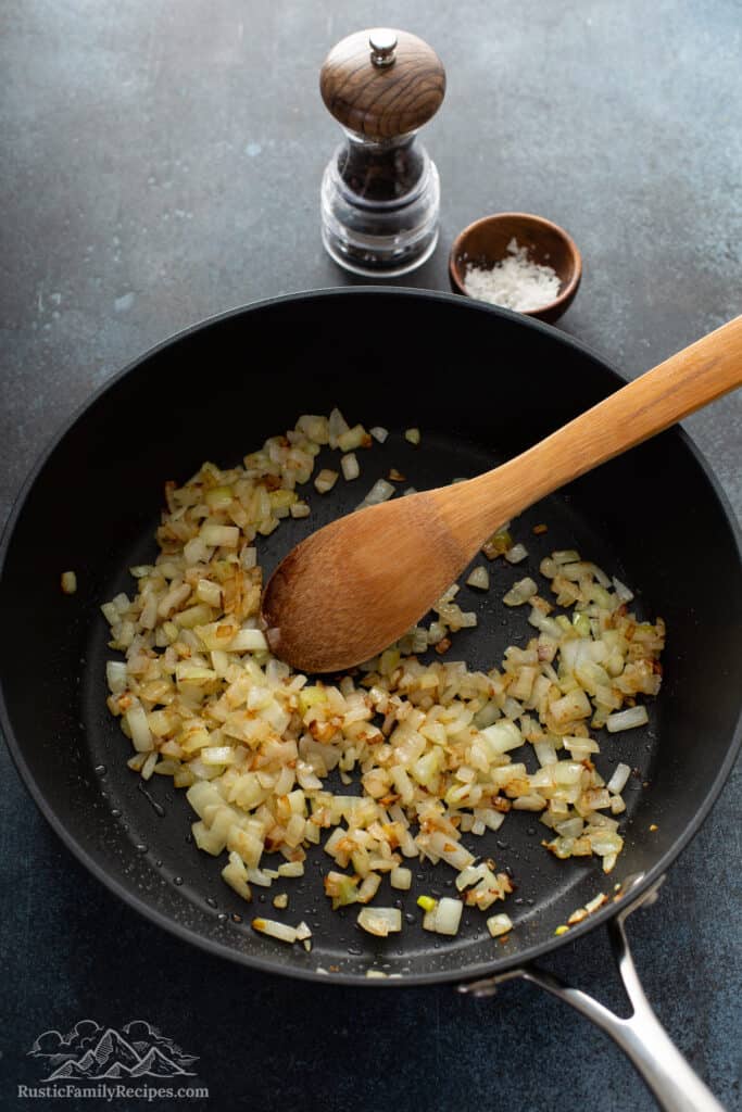 Diced onions being cooked in a pan with a wooden spoon