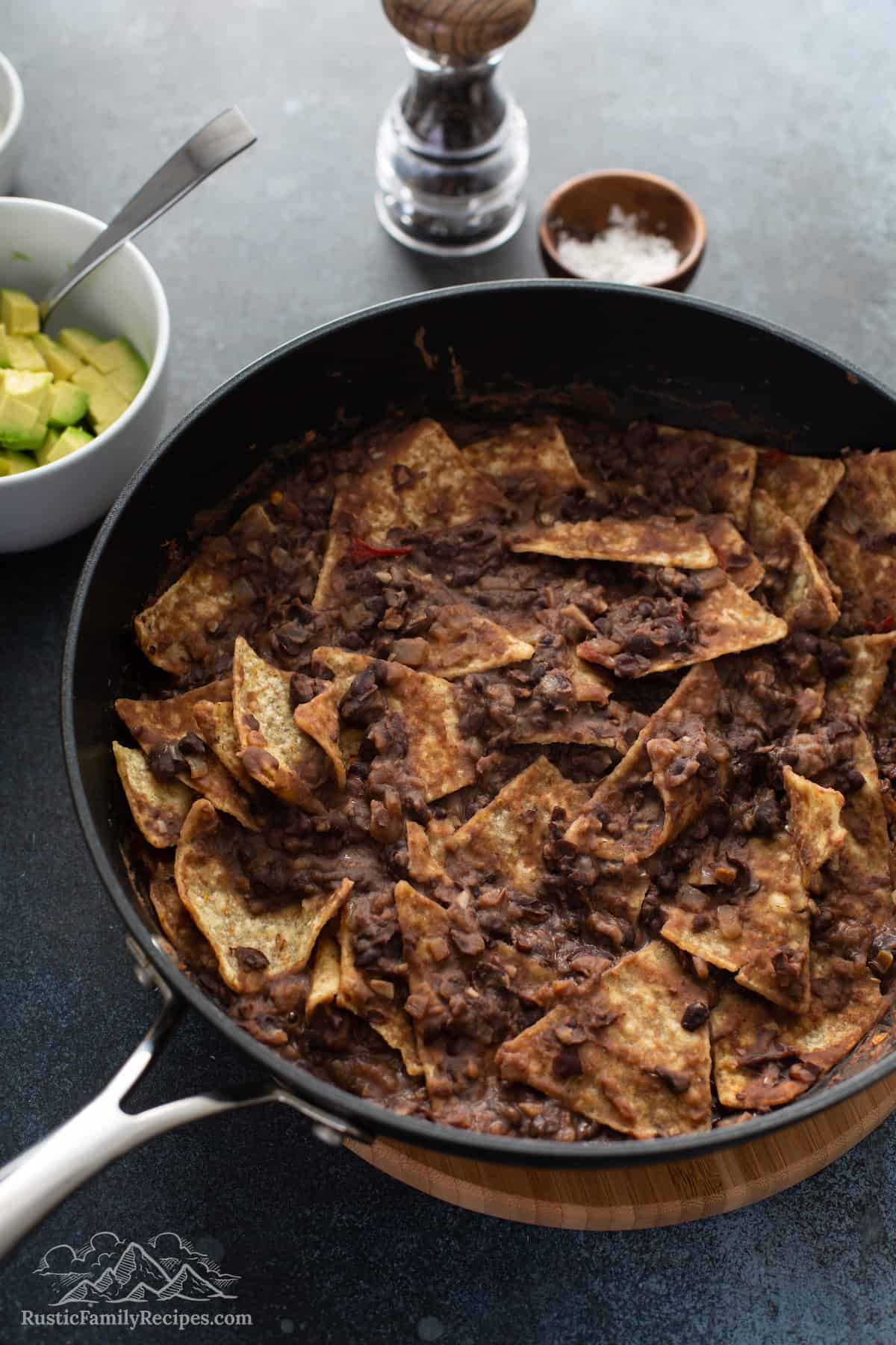 Tortilla chips mixed in with mashed black beans in a pan
