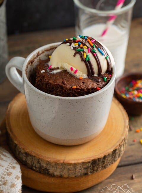 A chocolate cake in a mug topped with ice cream and sprinkles