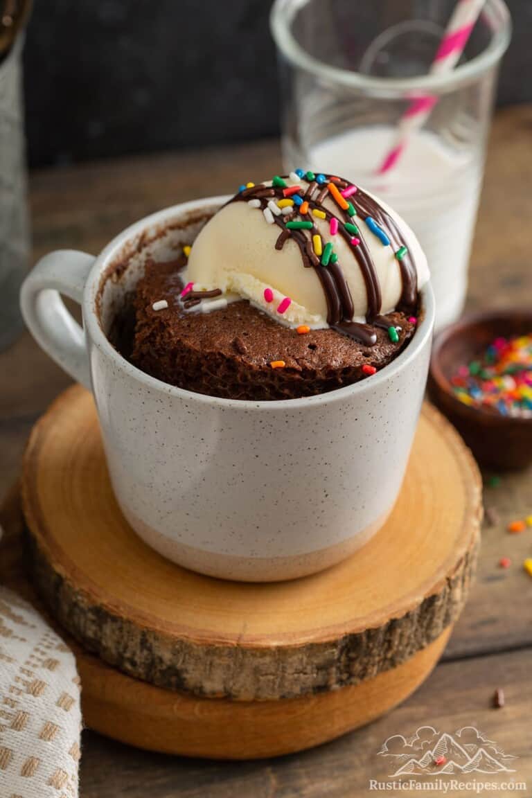 A chocolate cake in a mug topped with ice cream and sprinkles