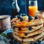 A stack of fluffy pancakes with blueberries, melted butter and syrup