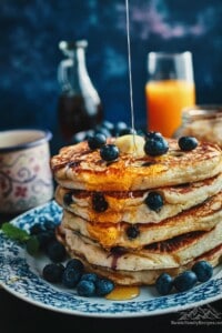 A stack of fluffy pancakes with blueberries, melted butter and syrup