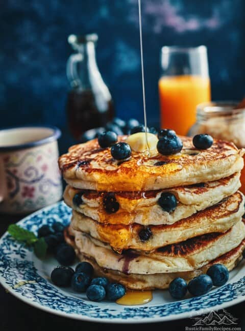 A stack of fluffy pancakes with blueberries, melted butter and syrup