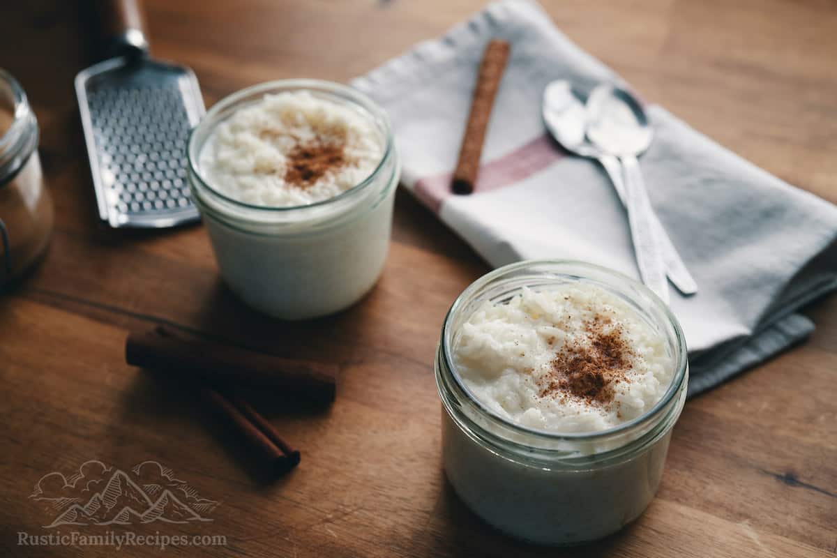 Homemade rice pudding in small mason jars topped with cinnamon, cinnamon sticks and microplane grater are nearby.