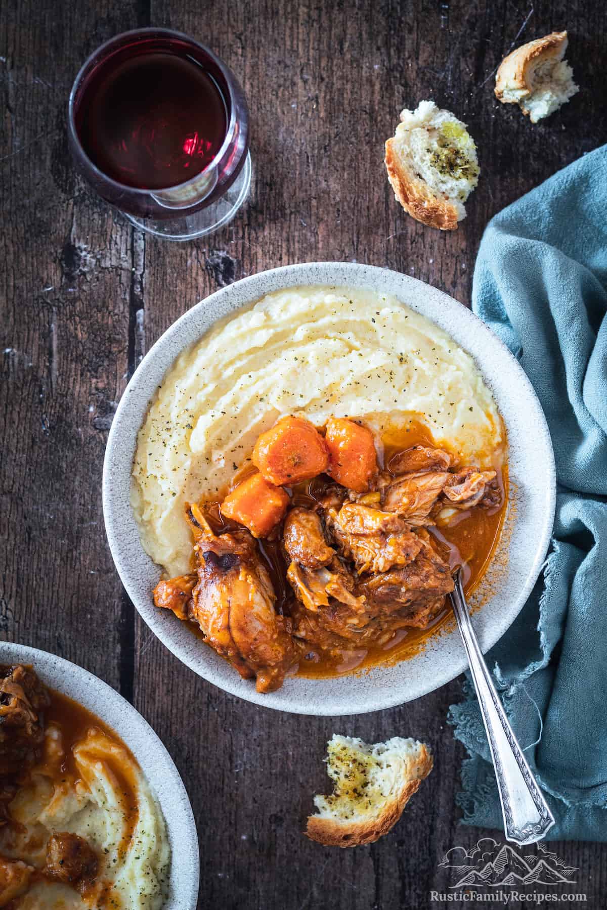A bowl filled with rabbit stew with mashed potatoes and a slice of bread