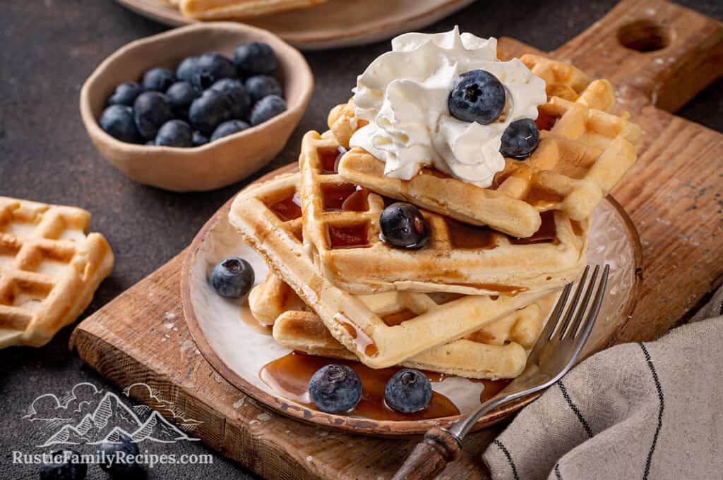 A stack of sourdough waffles topped with whipped cream and blueberries.