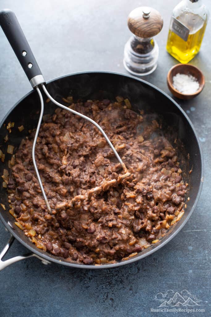 Pan of black beans with a masher.