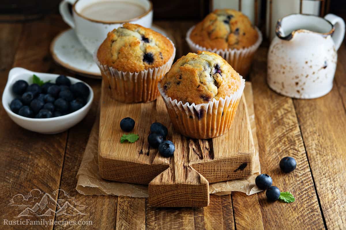 Three sourdough blueberry muffins on a wooden cutting board.