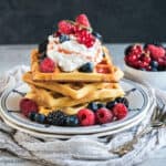 A plate with 3 sourdough waffles topped with berries and cream