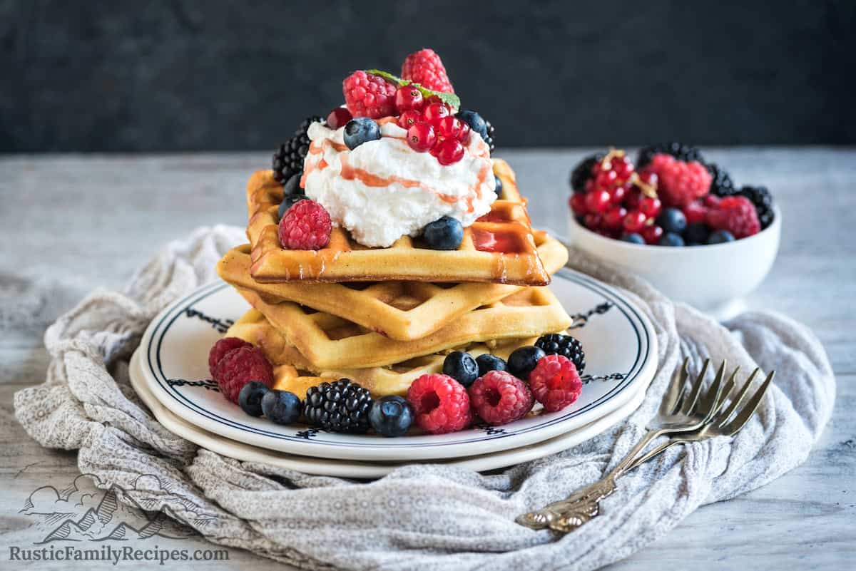 A plate with 3 sourdough waffles topped with berries and cream