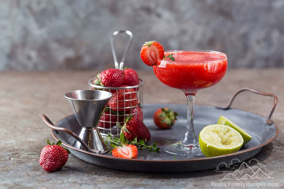 A frozen strawberry margarita with lime wedges and strawberries