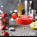 A frozen strawberry margarita with lime wedges and strawberries