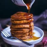 A stack of pumpkin corn cakes with syrup being poured
