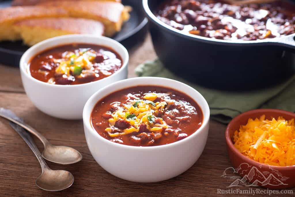 Two bowls of venison chili next to a bowl of cheese