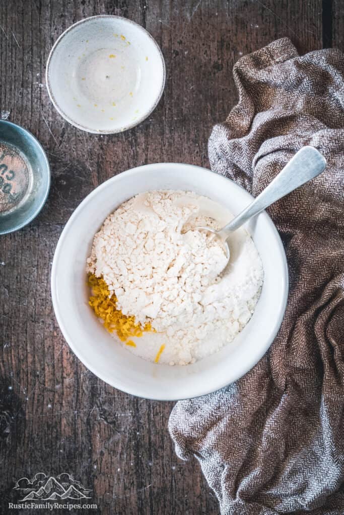 A white bowl with flour, sugar and lemon zest