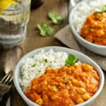 Two bowls of Instant Pot Sweet Potato Chickpea Masala with rice, a fork, and water.