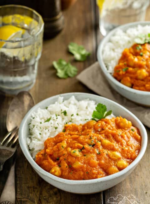 Two bowls of Instant Pot Sweet Potato Chickpea Masala with rice, a fork, and water.