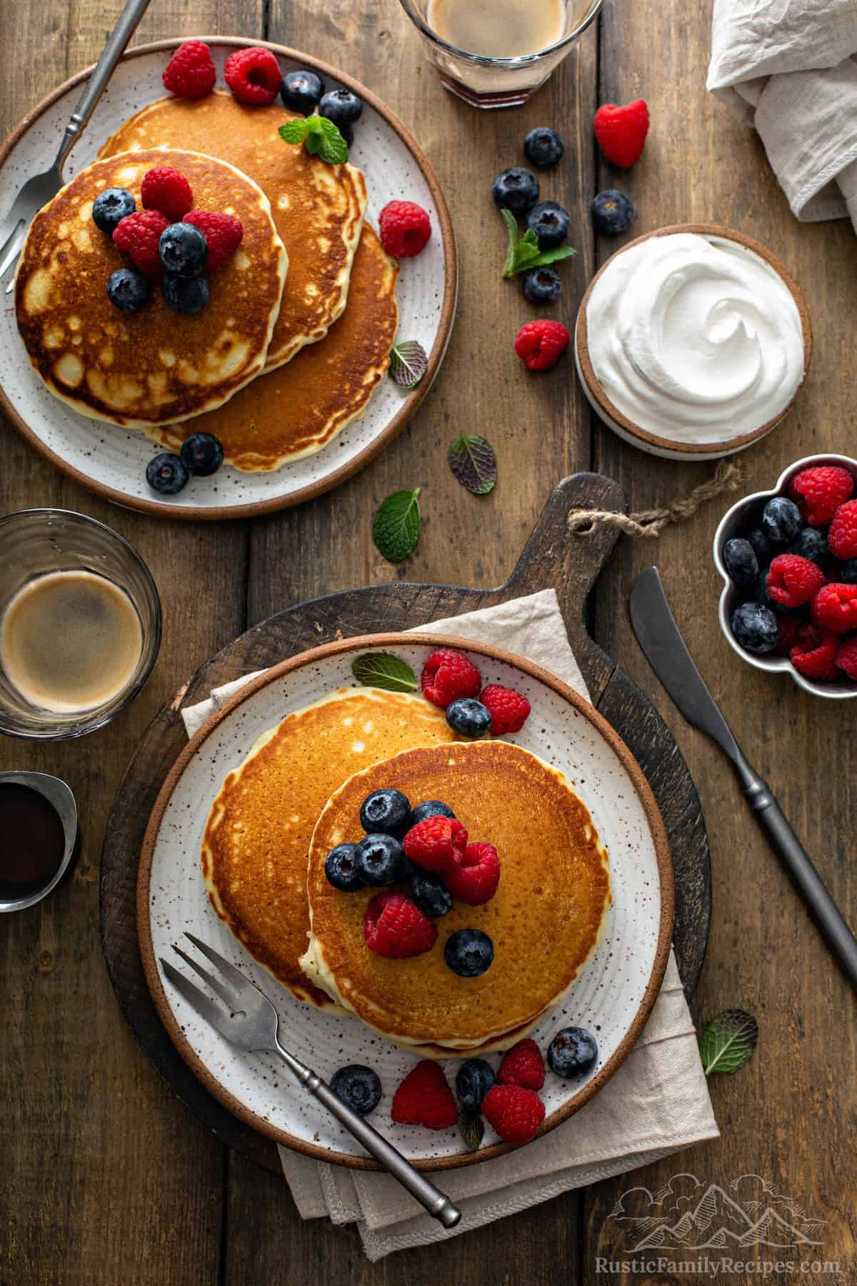Aerial view of two plates of fluffy pancake stacks topped with berries