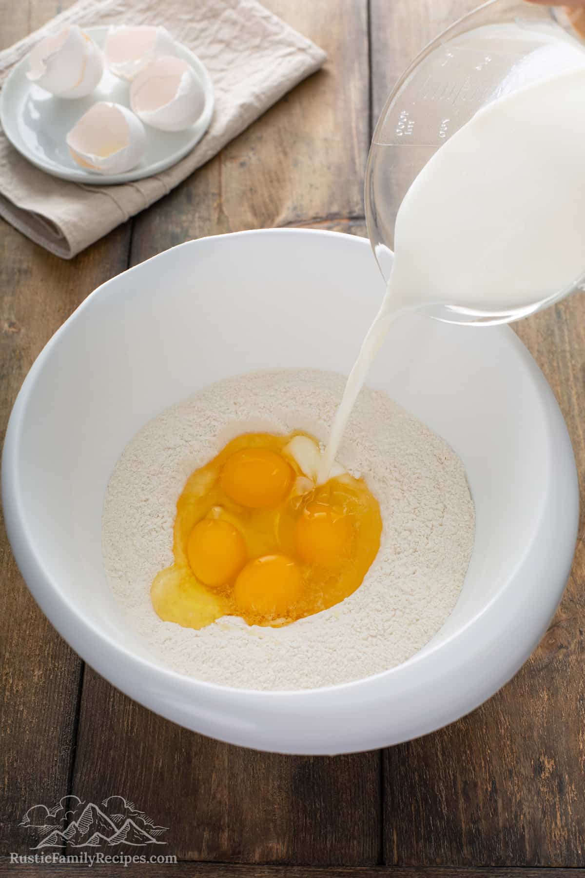 Milk being poured into a bowl with eggs and dry pancake ingredients